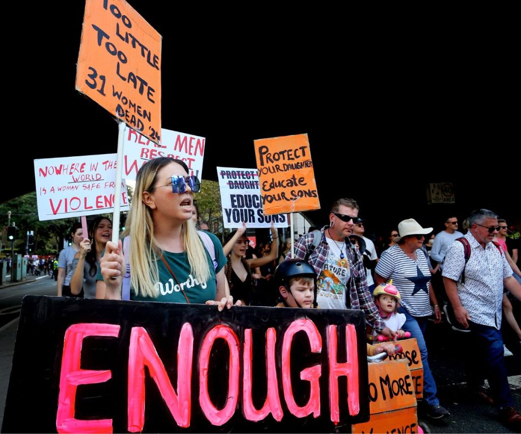 Protestors hold signs Too Little Too Late, 31 Women Dead '24, marching through city tunnel