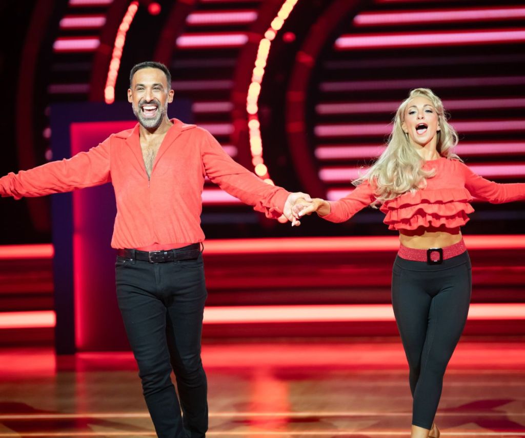 Adam and his dancing partner wear black pants and red shirts for their dance